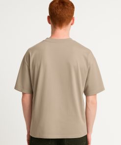 Modelo de espaldas con camiseta oversized beige sin diseño visible.