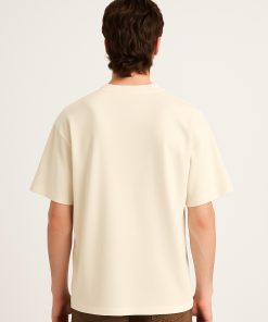 Modelo de espaldas usando camiseta oversized color crema sin gráficos.